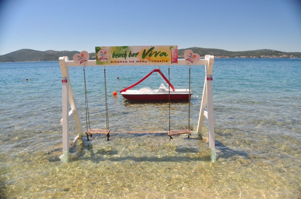 Huśtawki stojące w płytkiej wodzie przy Beach Bar Viva w Biogradzie