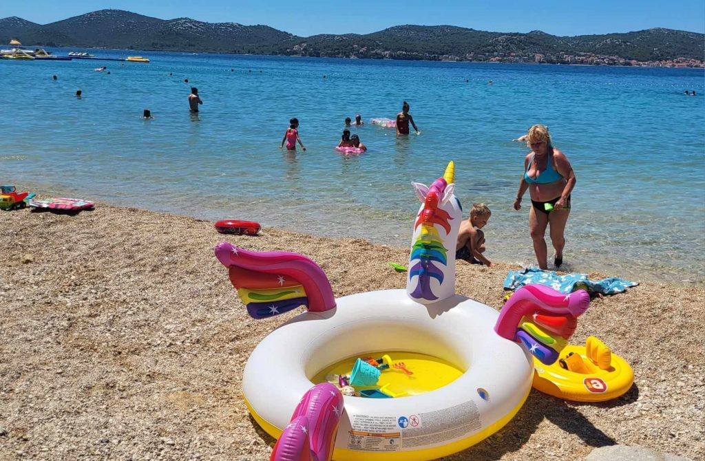 Dmuchany jednorożec i koła kąpielowe na żwirowej plaży nad Adriatykiem
